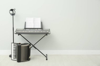 Electronic synthesizer, accordion and microphone near white wall indoors, space for text. Musical instruments clipart