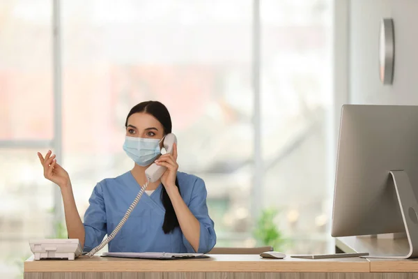 Recepciós Védő Maszkkal Beszél Telefonon Pultnál Kórházban — Stock Fotó