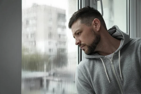 Depressed man near window at home. Space for text