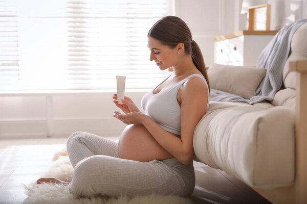 Молодая беременная женщина с косметическим продуктом дома
