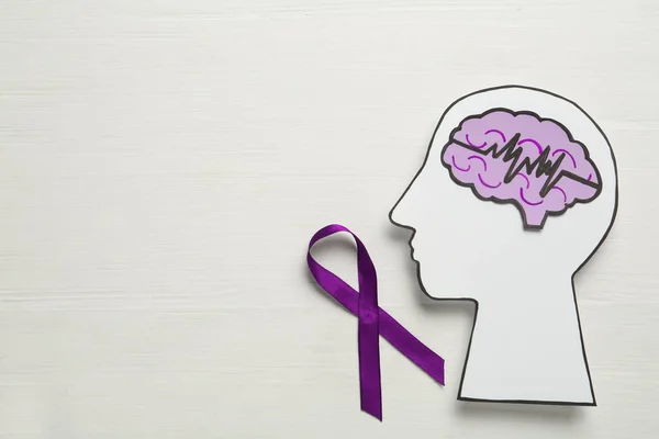 Human head cutout, brain and purple ribbon on white wooden background, flat lay with space for text. Epilepsy awareness