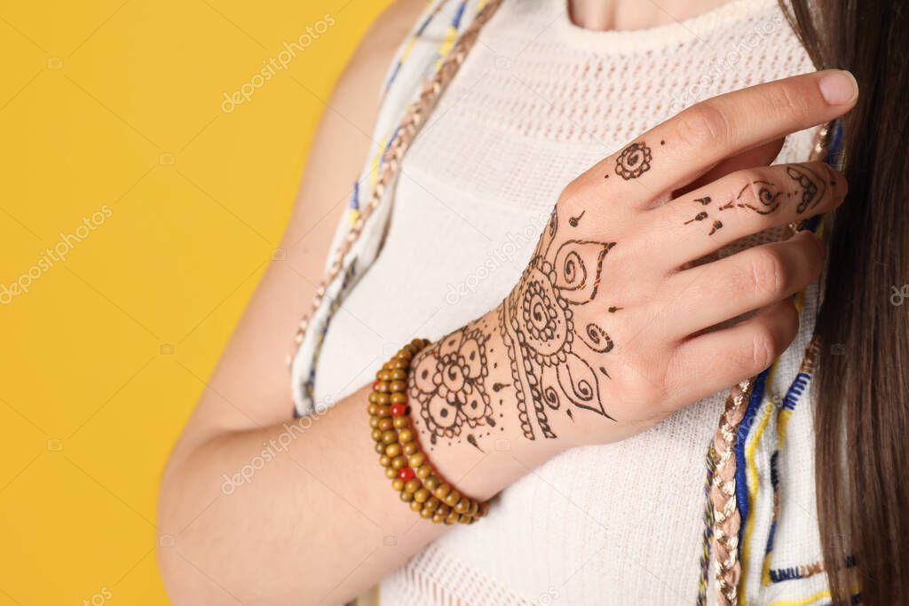 Woman with beautiful henna tattoo on hand against yellow background, closeup. Traditional mehndi