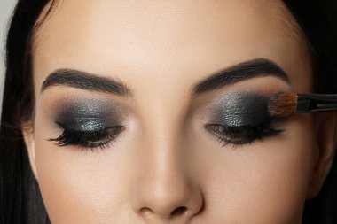 Applying dark eye shadow with brush onto woman's face, closeup. Beautiful evening makeup clipart