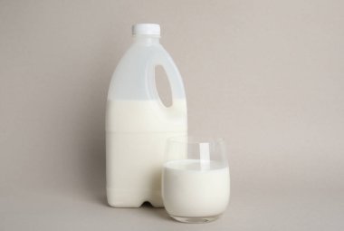 Bej arka planda bir şişe ve bir bardak süt.