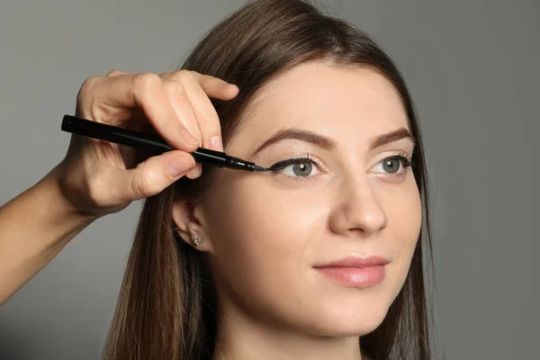 Konstnär Tillämpa Svart Eyeliner Kvinnans Ansikte Grå Bakgrund Närbild — Stockfoto