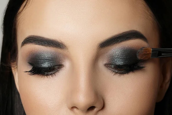 Applying dark eye shadow with brush onto woman\'s face, closeup. Beautiful evening makeup