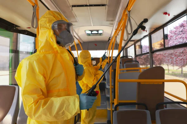 Public transport sanitation. Workers in protective suits disinfecting bus salon