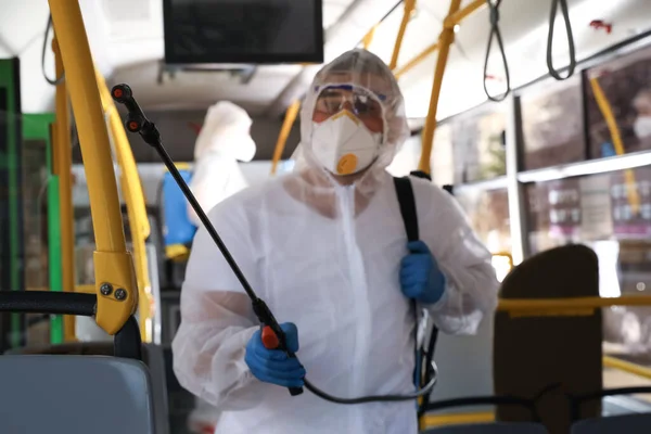 Public transport sanitation. Worker in protective suit disinfecting bus salon, focus on spray machine nozzle