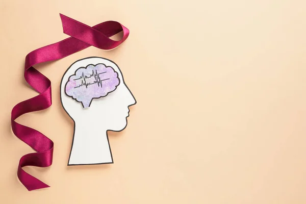 Human head cutout with brain near purple ribbon on beige background, flat lay. Epilepsy awareness