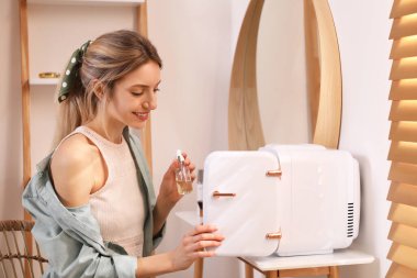 Kadın mini buzdolabından kozmetik ürünler alıyor.