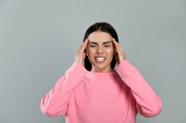Gri arka planda migren ağrısı çeken bir kadın.