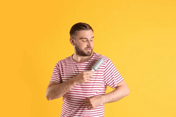 Young man cleaning clothes with lint roller on yellow background