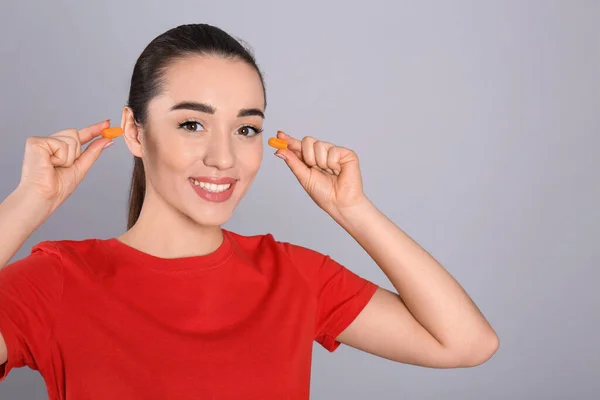 Młoda Kobieta Wkładająca Piankowe Zatyczki Uszu Szarym Tle — Zdjęcie stockowe