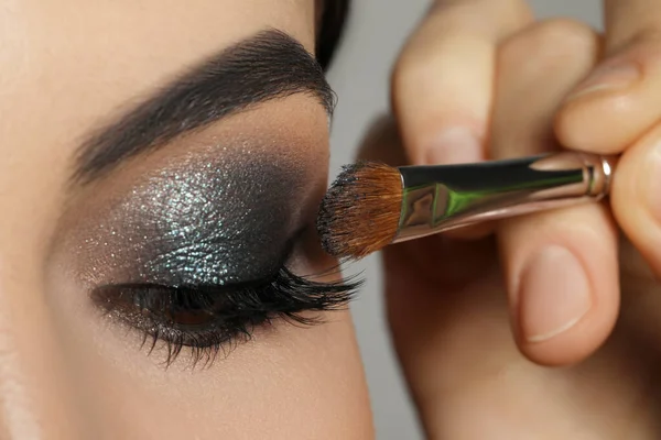 Applying dark eye shadow with brush onto woman\'s face, closeup. Beautiful evening makeup