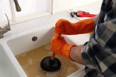 Lavaboyu açmak için lavabo pompası kullanan adam mutfaktaki gideri kapatıyor.
