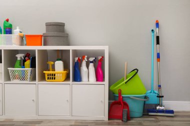 Açık gri duvarın yanında deterjan ve temizlik aletleri olan raf ünitesi.