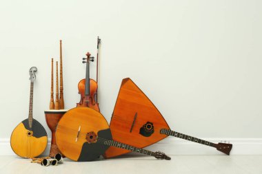 Beyaz duvarın yanında farklı ahşap müzik aletleri var.