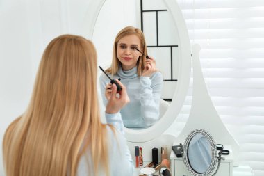 Güzel bir kadın aynanın yanında makyaj yapıyor.