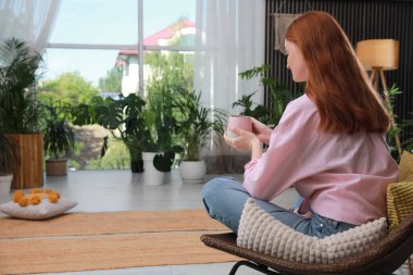 Kapalı terastaki koltukta oturan bardaklı kadın.