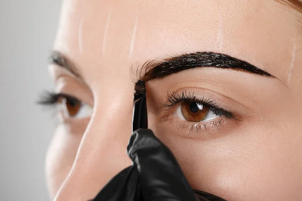 グレーの背景に眉毛の矯正手順の間に色合いを適用する美容師 クローズアップ — ストック写真