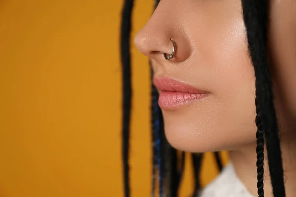 Young woman with nose piercing on yellow background, closeup. Space for text