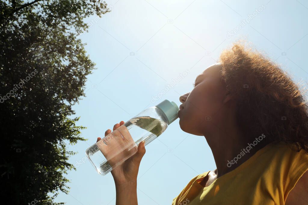 African-American woman drinking water to prevent heat stroke outdoors