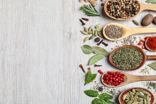 Different natural spices and herbs on light wooden table, flat lay. Space for text