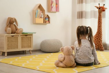 Oyuncak ayıyla evde yerde oturan yalnız küçük bir kız. Otizm kavramı