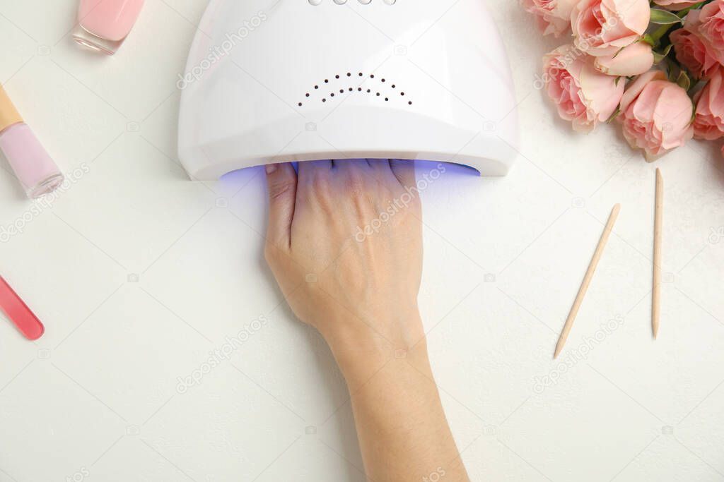 Woman using ultraviolet lamp to dry gel nail polish at white table, top view