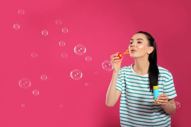Pembe arka planda sabun köpüğü üfleyen genç kadın, mesaj için boşluk