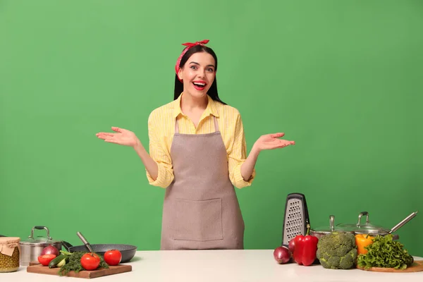 Эмоциональная Домохозяйка Белым Столом Овощами Различной Посудой Зеленом Фоне — стоковое фото