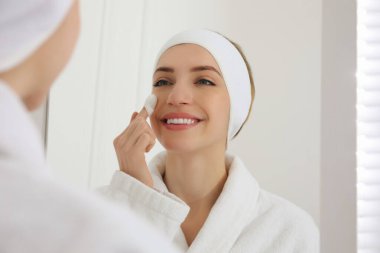 Evde aynanın yanında deri bakımında ipek böceği kozası kullanan bir kadın.