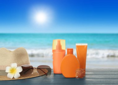 Farklı cilt güneş koruma ürünleri ve deniz manzarasına karşı mavi ahşap masa üzerindeki plaj aksesuarları. Tasarım için boşluk