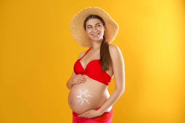 若いです妊娠中の女性とともに太陽保護クリームオン腹上の黄色の背景 — ストック写真