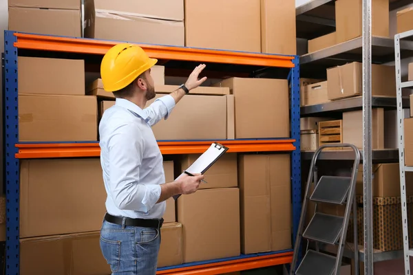 Jonge Man Met Klembord Buurt Van Rek Van Kartonnen Dozen — Stockfoto