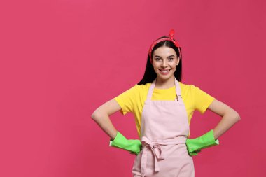 Pembe arka planda lastik eldiven takan genç bir ev hanımı.