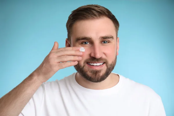 Happy Young Man Applying Facial Cream Light Blue Background — Stock Photo, Image