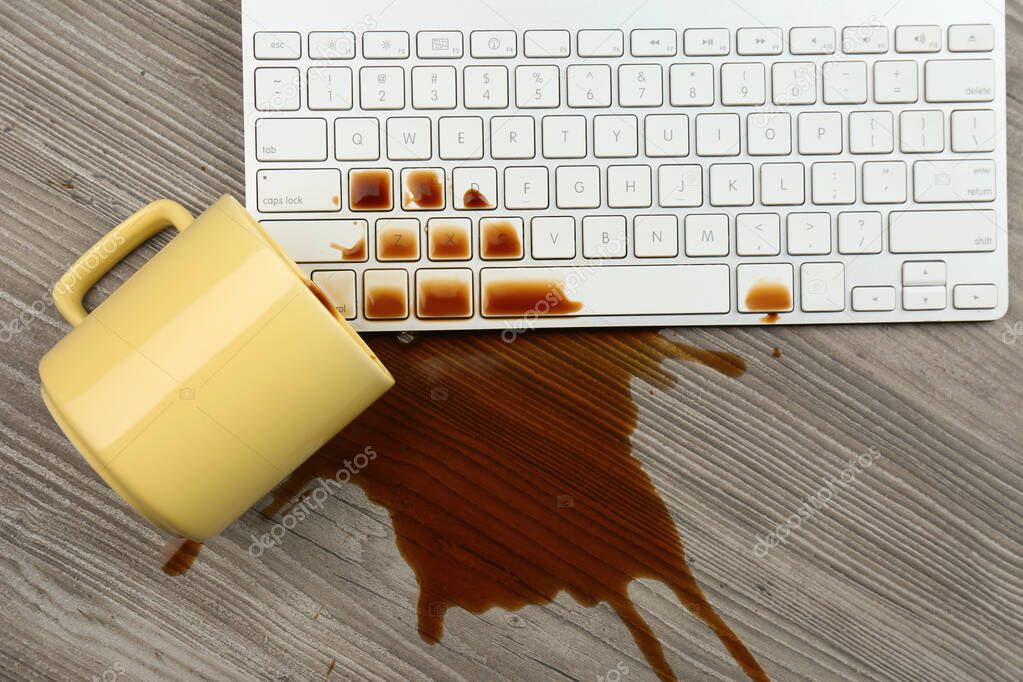 Cup of coffee spilled over computer keyboard on wooden table, flat lay