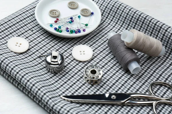 Beyaz ahşap masa üzerinde farklı dikiş malzemesi ve kumaş bileşimi.