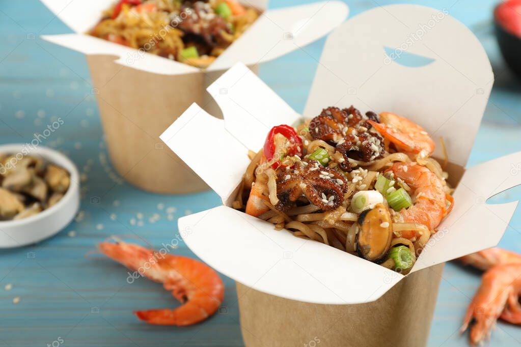 Boxes of wok noodles with seafood on light blue wooden table, closeup