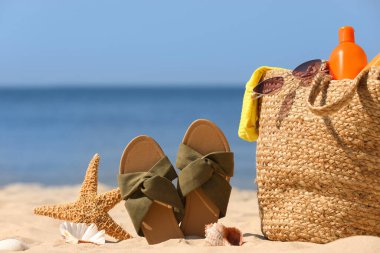 Kumsal aksesuarları ve deniz kenarındaki kumlarda terlikleri olan çantalar.