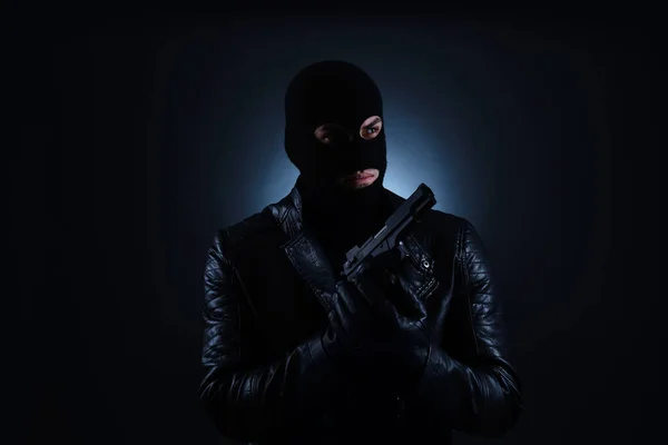 Man wearing knitted balaclava with gun on black background