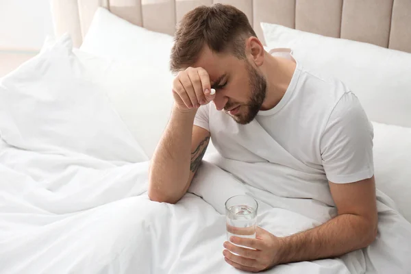 有一杯水和药丸的男人在床上得了偏头痛 — 图库照片