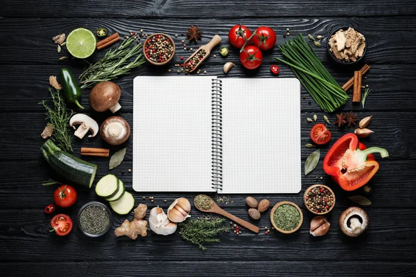 Open recipe book and different ingredients on black wooden table, flat lay. Space for text