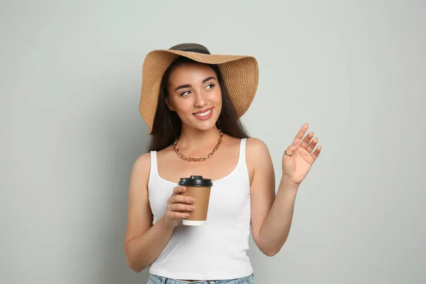薄い灰色の背景に麦藁帽子とコーヒーカップを持つ美しい若い女性 スタイリッシュなヘッドアドレス — ストック写真