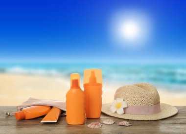 Different skin sun protection products and hat on wooden table against seascape. Space for design