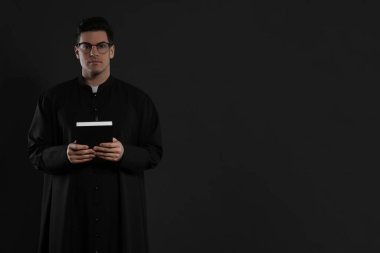 Siyah arka planda İncil 'i olan bir rahip. Metin için boşluk