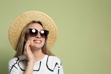 Açık yeşil arka planda hasır şapka ve güneş gözlüğü takan güzel genç bir kadın. Mesaj için yer var. Şık başlık
