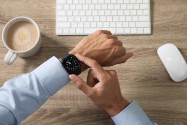 MYKOLAIV, UKRAINE - OCTOBER 04, 2019: Man using Apple Watch to check time at wooden table, top view