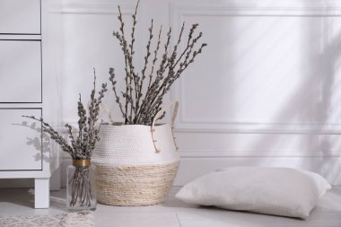 Pussy willow tree branches and pillow near chest of drawers in room